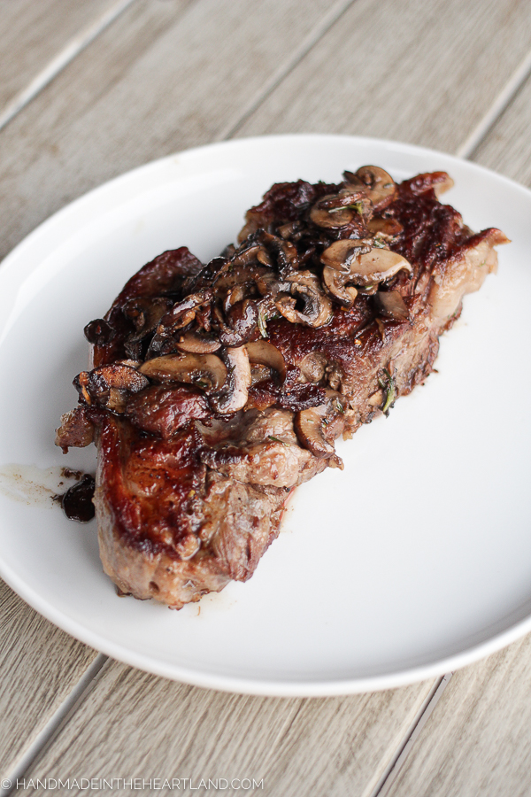 A ribeye steak with mushrooms on top sitting on white plate