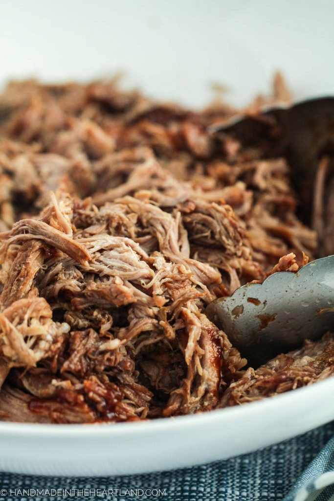 image of pulled pork with bbq sauce in a bowl with tongs to serve