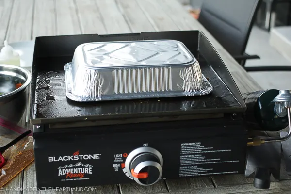 aluminum pan covering food cooking on a blackstone outdoor griddle