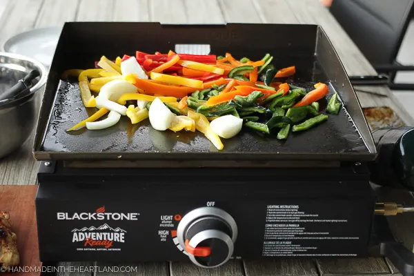bell peppers, poblano peppers and onions cooking on a Blackstone griddle outside