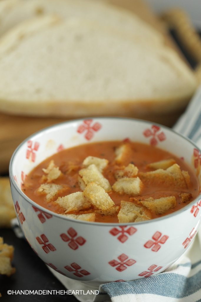 A bowl with tomato soup with croutons and sourdough bread in background