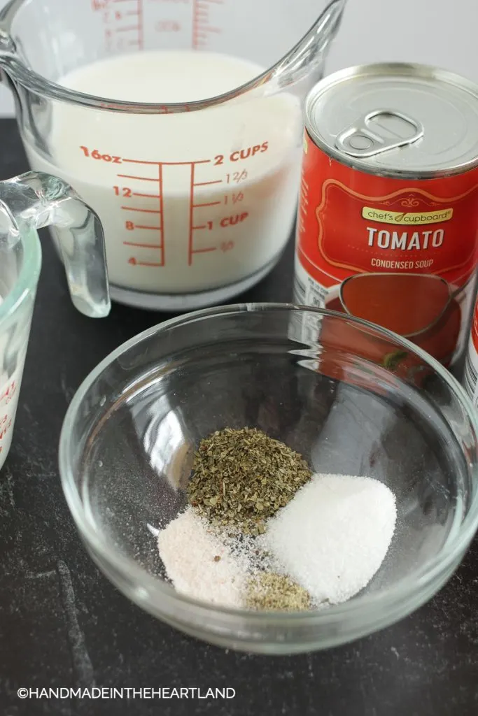 ingredients for tomato soup: spices in a glass bowl with milk and tomato canned soup in background