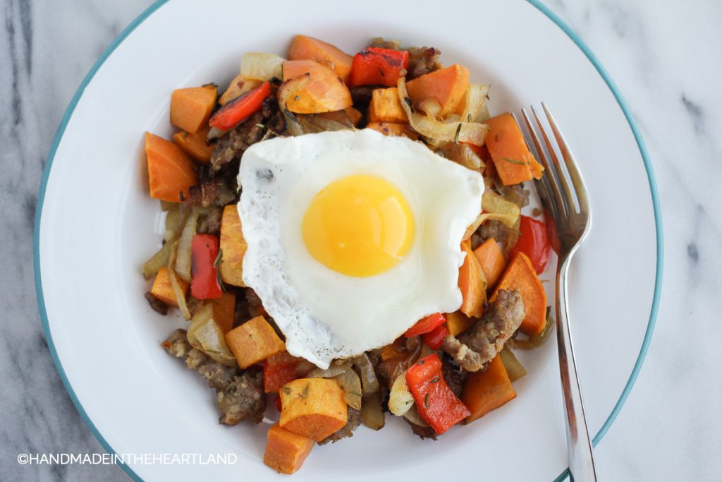 sausage, onions, bell peppers and sweet potatoes, roasted on a plate with sunny side egg on top
