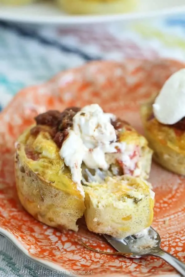 Egg muffin topped with salsa and sour cream on an orange plate