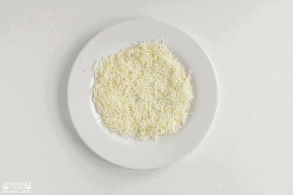 shredded cheese on a white plate ready to roll a cheeseball into