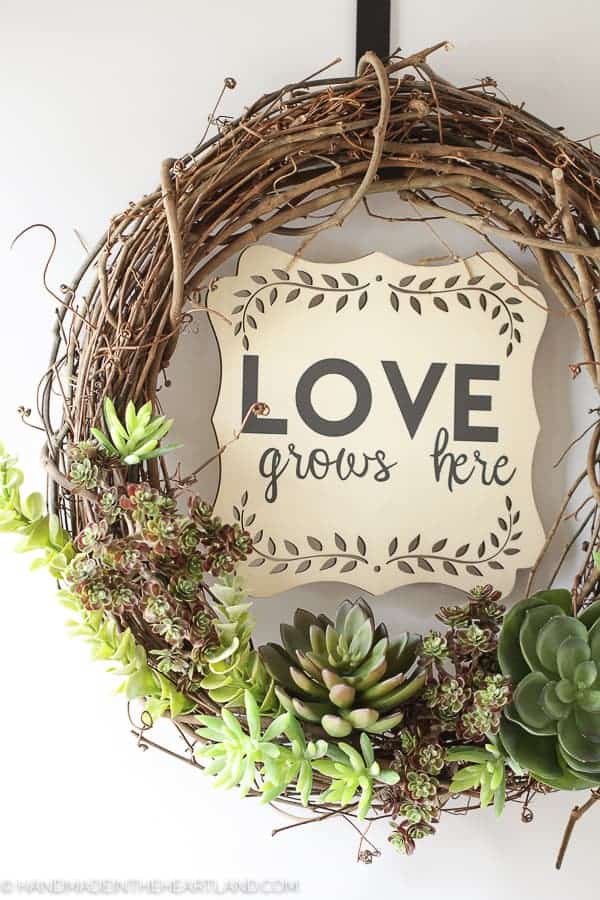 grapevine wreath with faux succulents on the bottom and "love grows here" on a wood piece in center