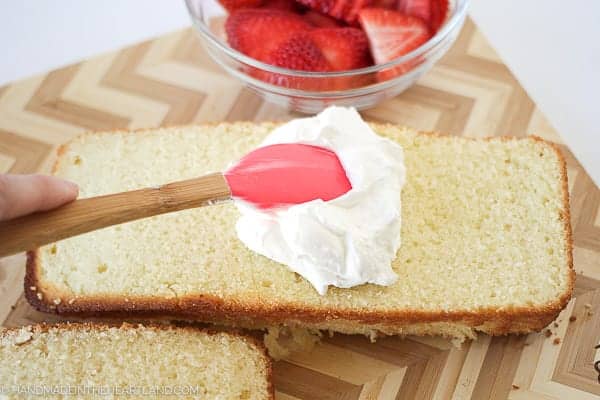 spreading whipped cream on strawberry shortcake cake