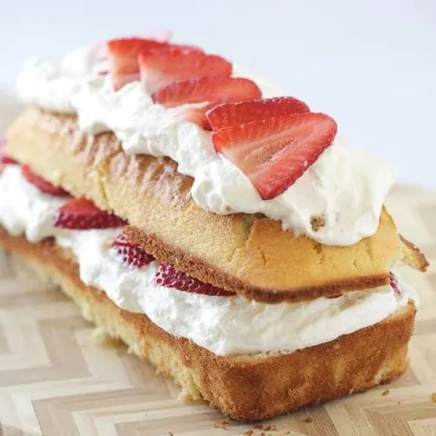 A pound cake loaf, cut in half lengthwise with strawberries and whipped cream in the center and on top