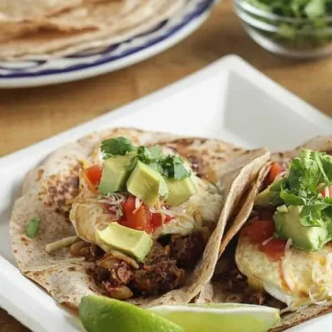 two tacos with red beans, avocado, salsa and limes on a white plate