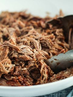 image of pulled pork with bbq sauce in a bowl with tongs to serve