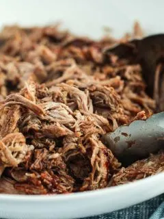 image of pulled pork with bbq sauce in a bowl with tongs to serve