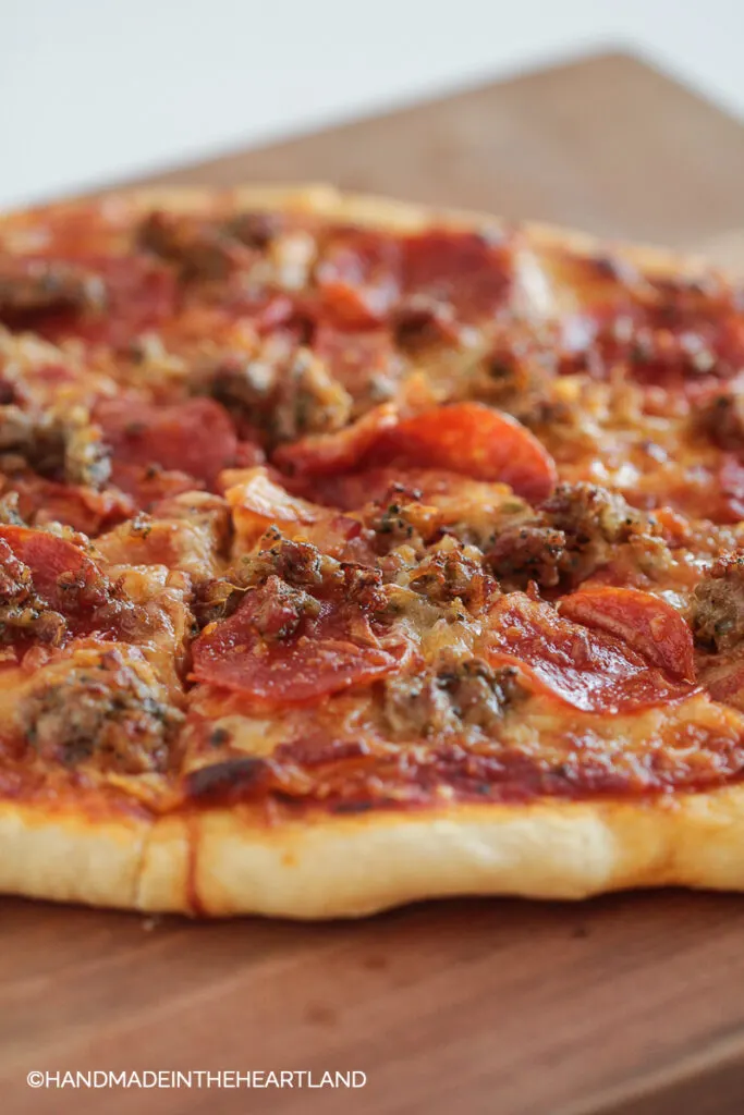 sliced pizza with meat toppings sitting on a wood cutting board