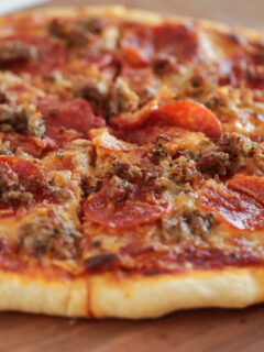 Sliced homemade pizza with 3 meat toppings sitting on wood cutting board