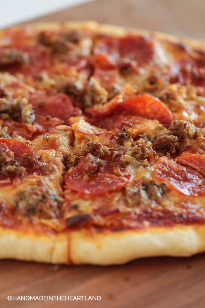 Sliced homemade pizza with 3 meat toppings sitting on wood cutting board