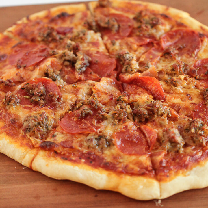 meat lovers pizza sitting on a wood cutting board sliced.