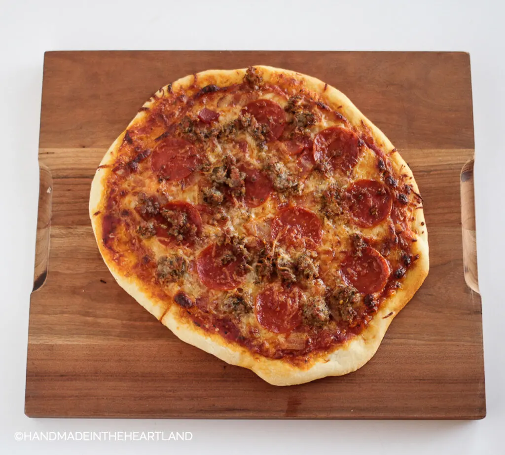 homemade pizza with pepperoni, sausage and bacon sitting on a wood cutting board