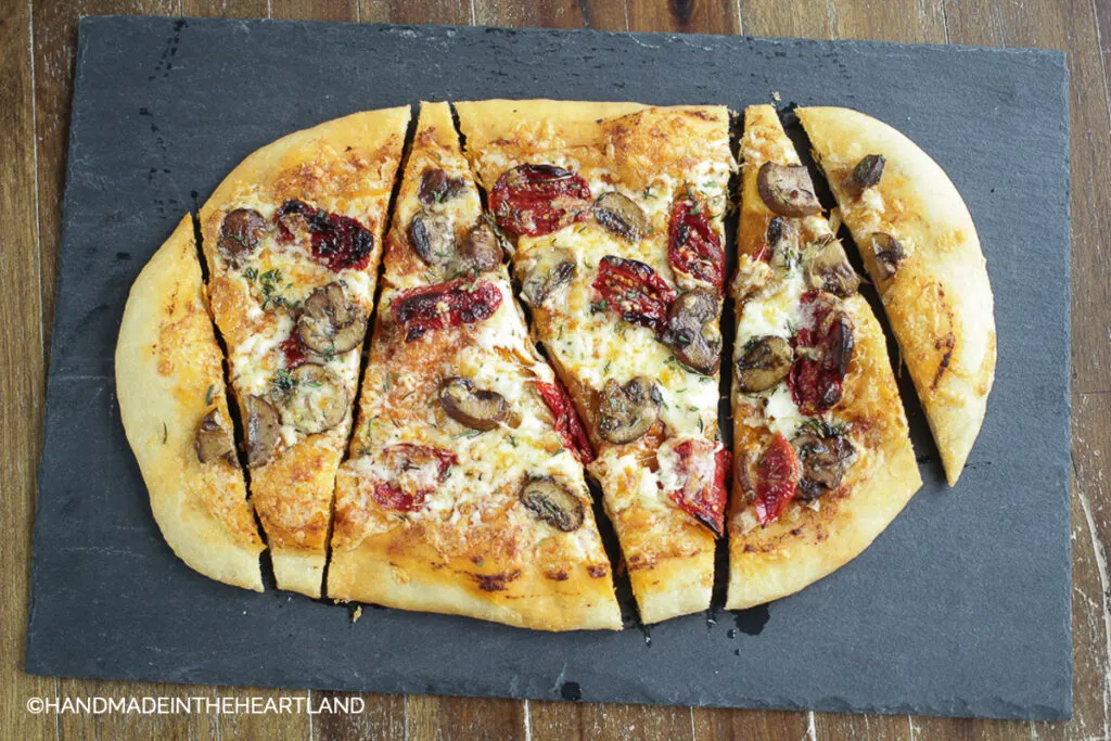 oval shaped pizza with mushrooms and sun-dried tomatoes on dark slate serving board