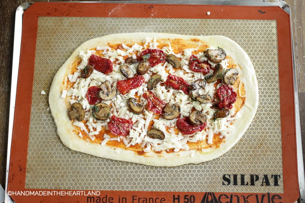 Mushroom and Sun-dried tomato pesto pizza before it goes into the oven, sitting on Silpat nonstick baking liner