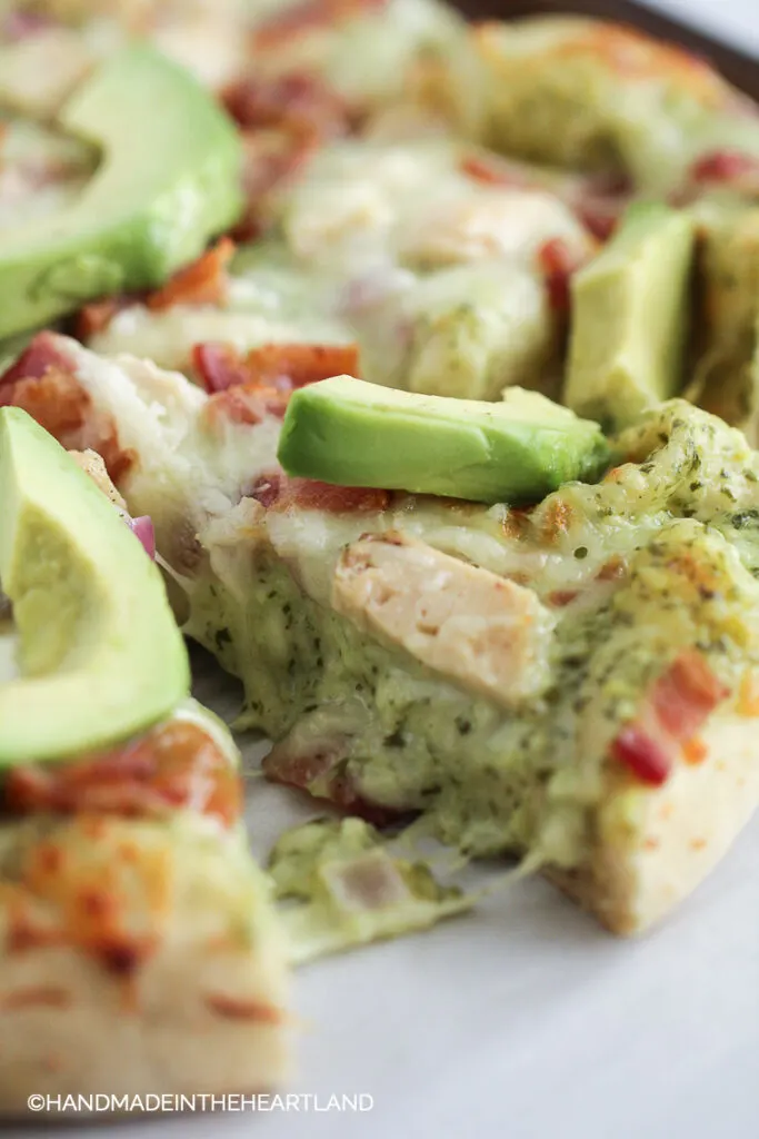 Pizza slice with melty cheese, chicken, and avocado on top