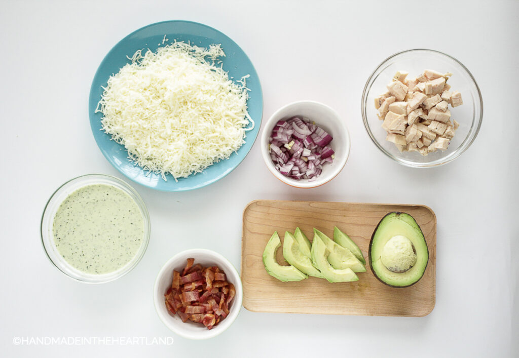 Ingredients for topping a bacon chicken ranch pizza on a white background