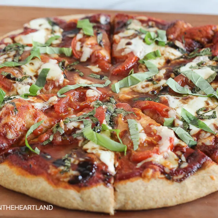 Circle Pizza with fresh mozzarella, basil and tomatoes with red sauce sitting on cutting board