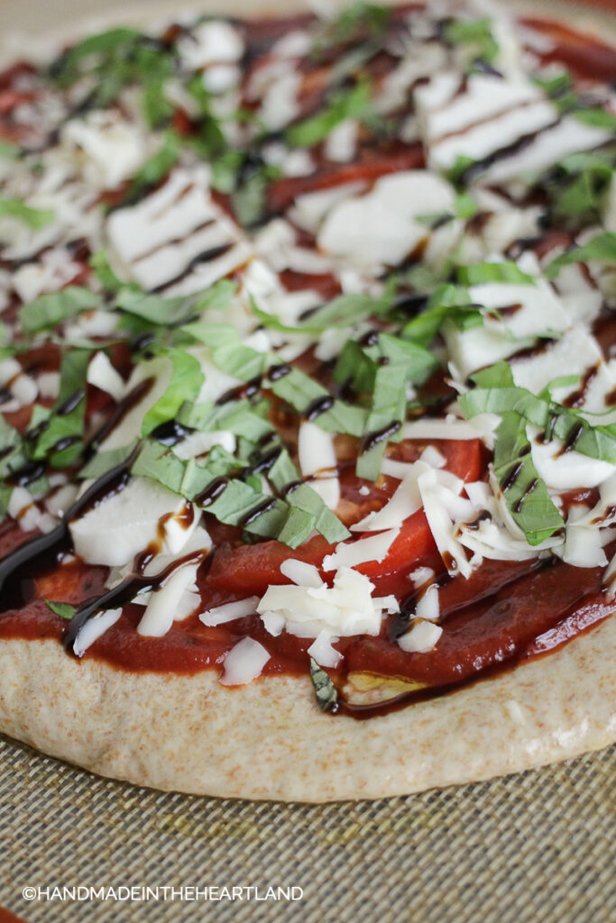 caprese pizza before its cooked, sitting on silpat nonstick baking liner