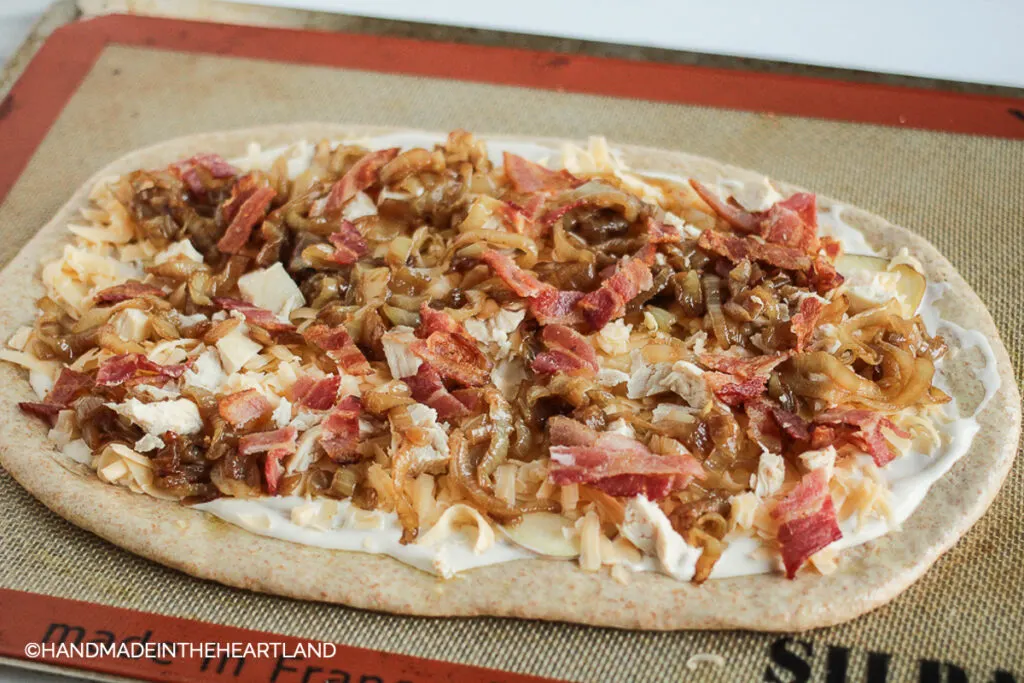 homemade pizza before going into the oven with toppings of chicken, bacon, apples, caramelized onions and alfredo sauce