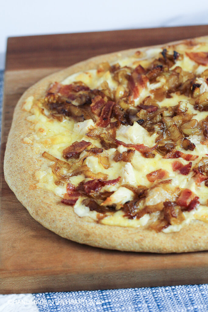 Homemade pizza with chicken, apples and caramelized onions sitting on a cutting board