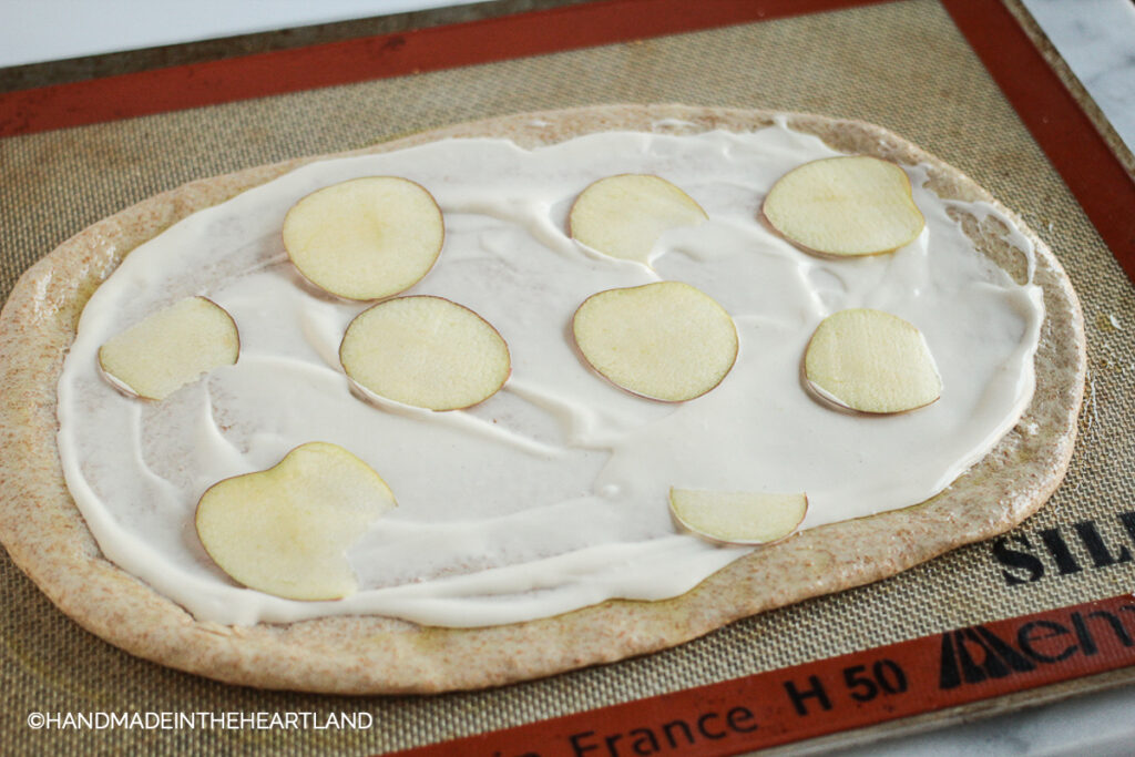 thinly sliced apple rounds on top of alfredo sauce on pizza crust