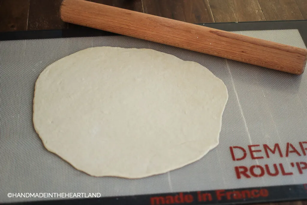 pizza dough sitting on roulpat mat with rolling pin