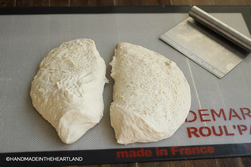 pizza dough sitting on a roul'pat silicone counter mat with silver metal pastry cutter