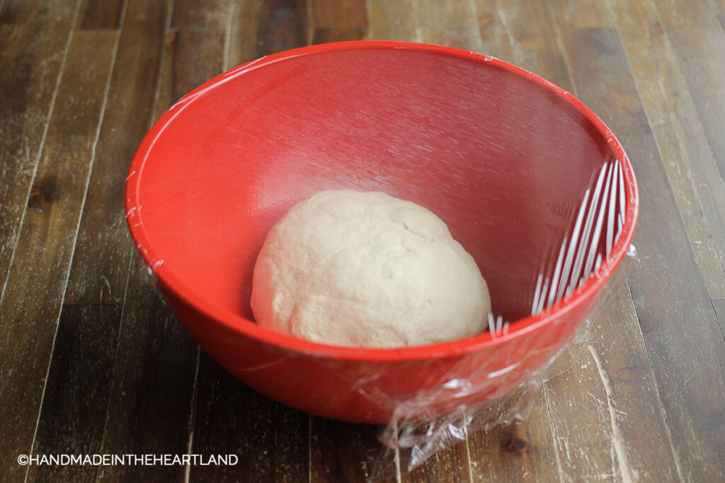 Pizza dough in bowl covered with plastic wrap