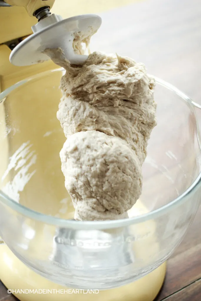 pizza dough mid way through mixing attached to dough hook of a stand mixer