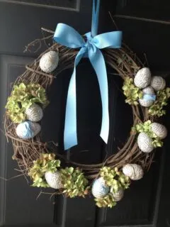 Easter wreath hanging on a black front door with Easter eggs, hydrangeas and ribbon