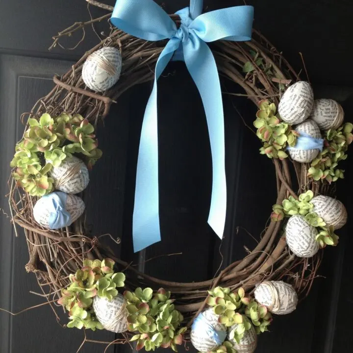 Easter wreath hanging on a black front door with Easter eggs, hydrangeas and ribbon