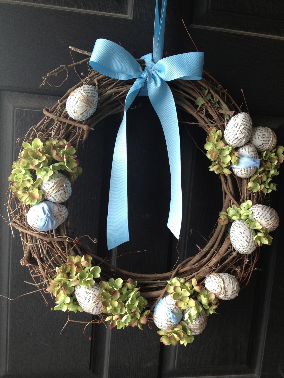 Easter wreath hanging on a black front door with Easter eggs, hydrangeas and ribbon