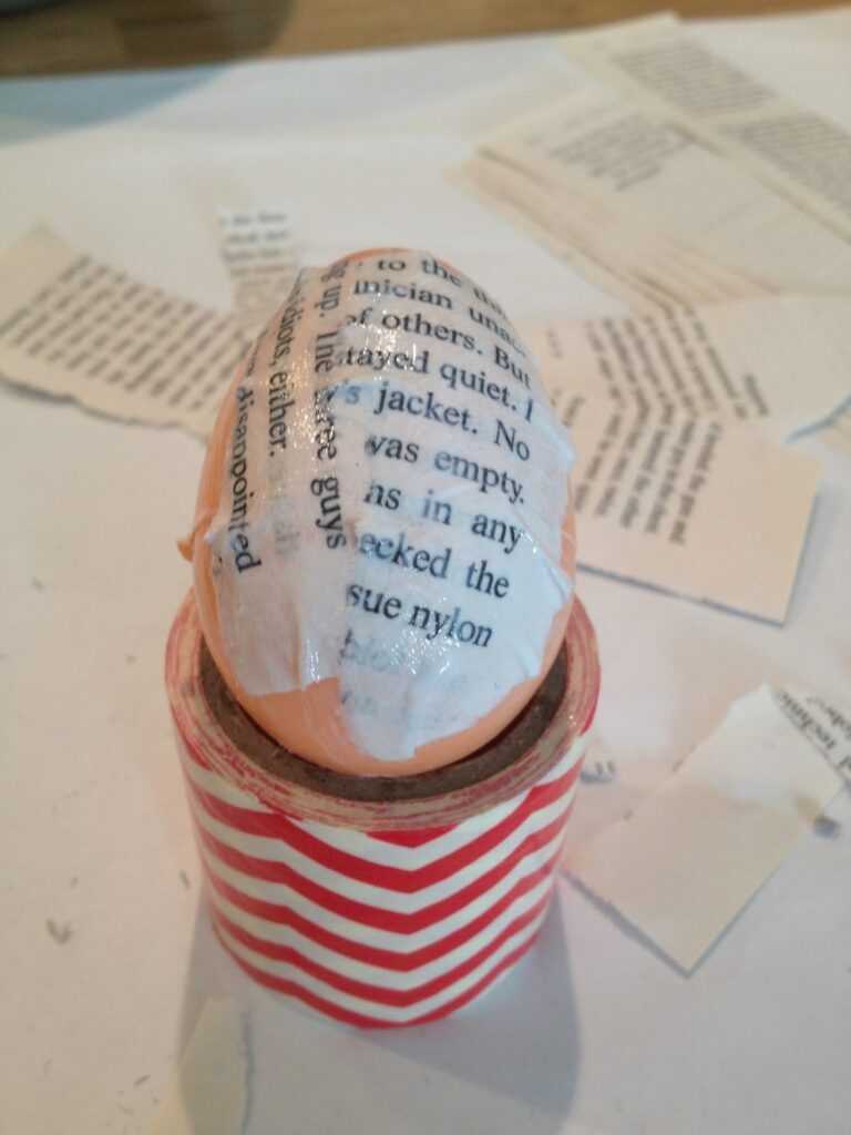 In process decoupage of applying pieces of book pages to a plastic easter egg