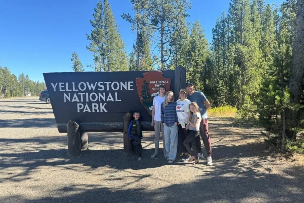Family of 6 standing in front of the Yellowstone national park entrance sign